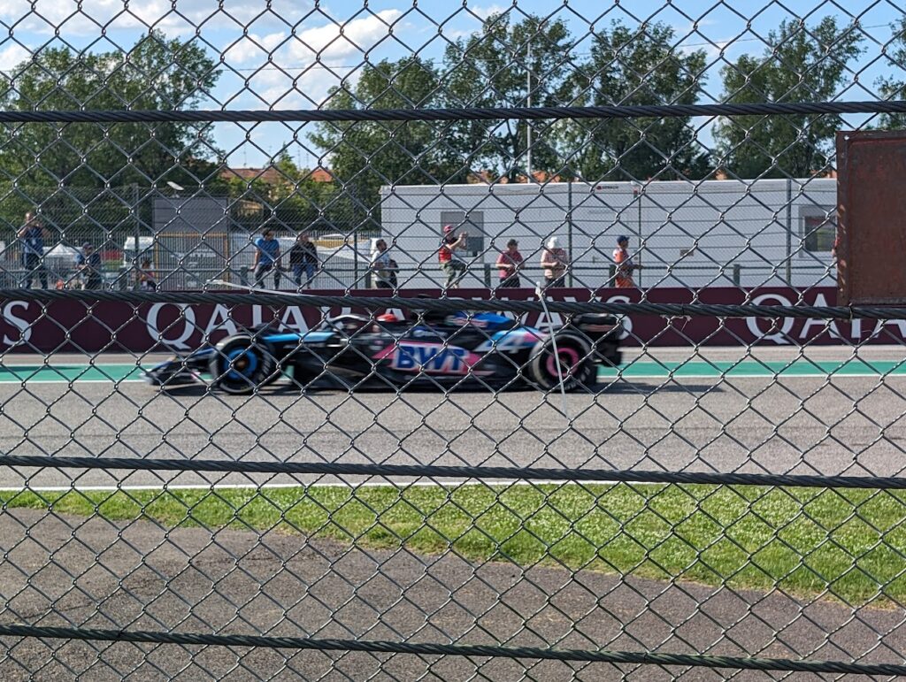 An Alpine driver speeds by in front of the RIvazza 1 grandstands as viewed from the GA area.