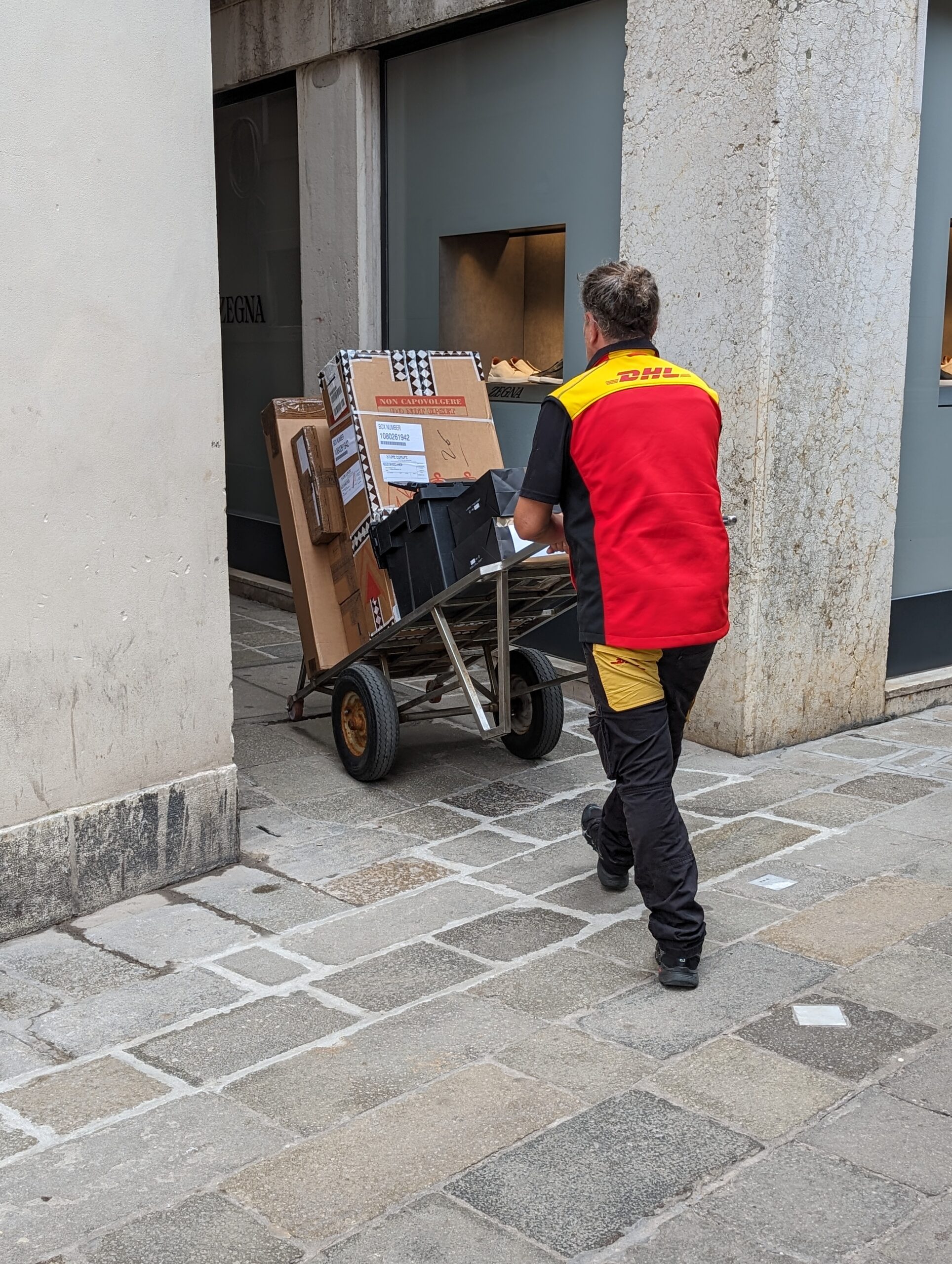 A DHL delivery man pushing a hand-truck full of packages through the streets of Venice.