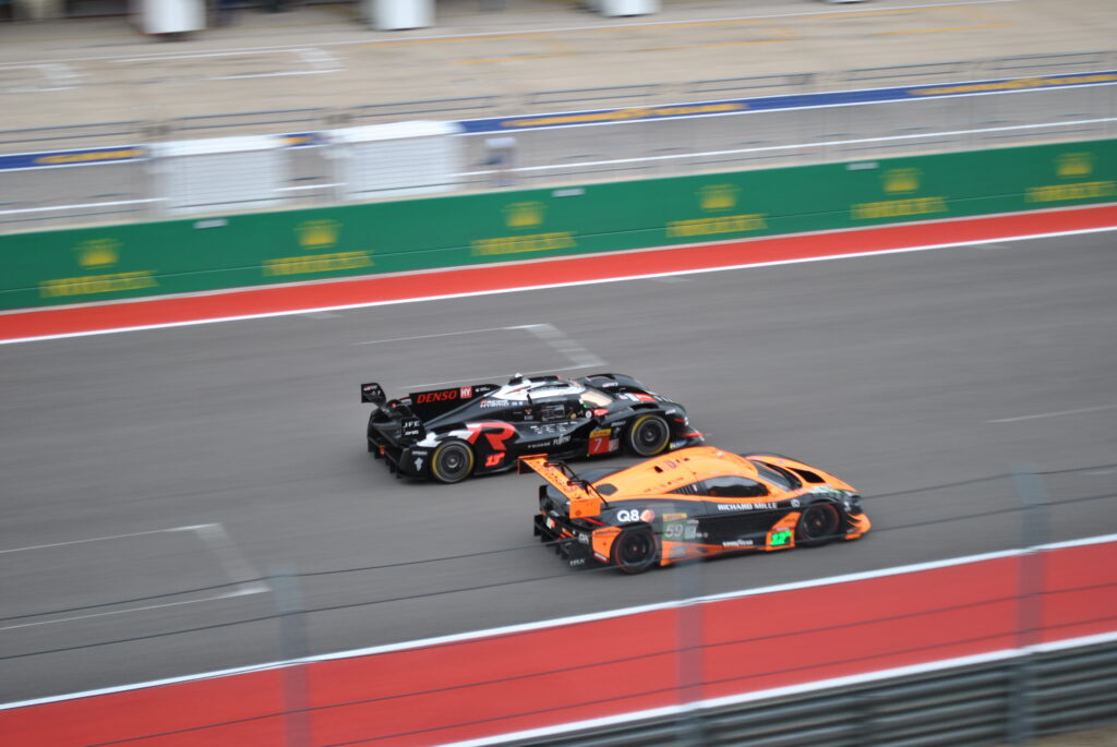 View from the middle of the Club section of the Main Grandstands of some mixed class racing down the main straight.