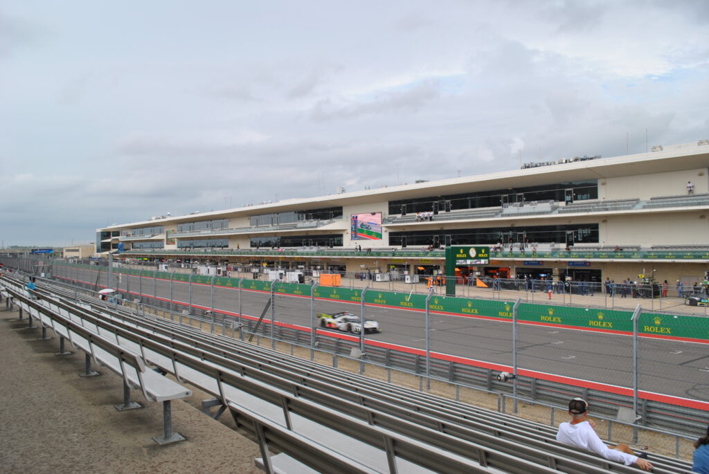Trackside bleachers (left) view towards T20 and a Peugeot Hypercar streaking down the straight.