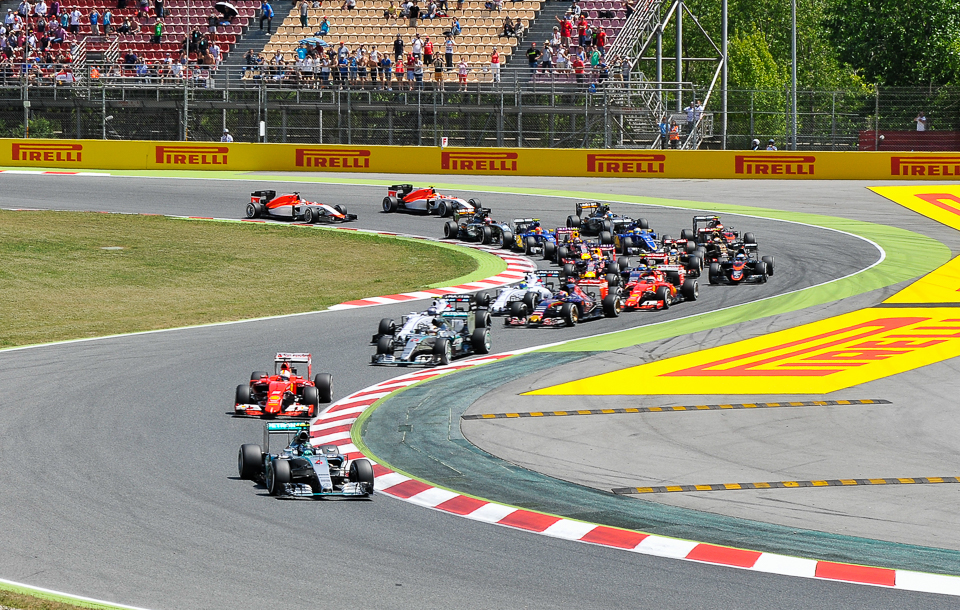 Wide-angle shot of the race start at the 2015 Spanish Grand Prix, showing the full grid of Formula 1 cars accelerating from the starting line into the first corner at Circuit de Barcelona-Catalunya.